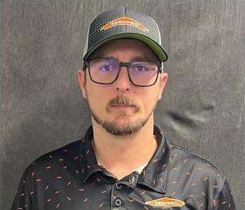 Grumpy male person with with brown short mustache and beard, with glasses, wearing a ballcap and black shirt  