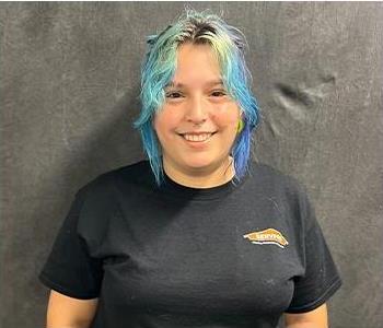 Happy smiling girl wearing a black shirt with fun blue-black-gold hair wearing a black shirt in front of grey screen.