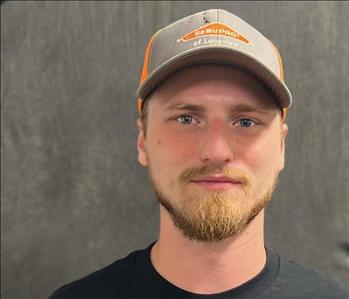 Male person  with short light brown beard with piercing blue eyes wearing a black shirt and ballcap.