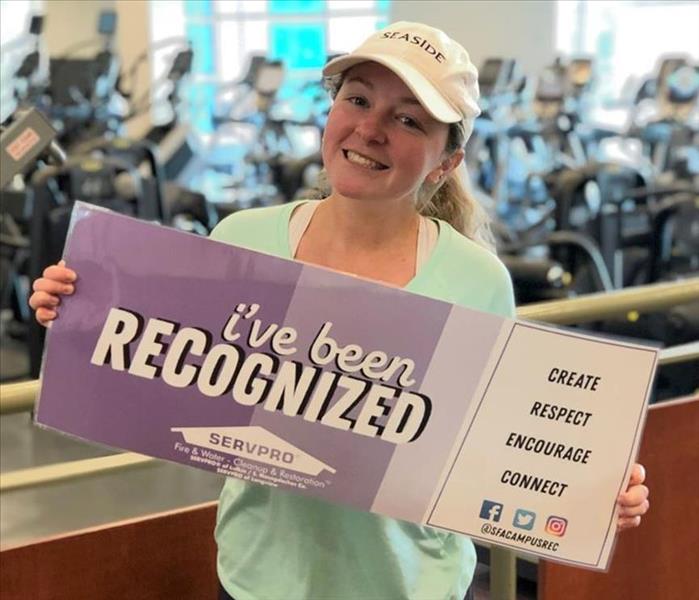 A woman standing in a gym with a SERVPRO branded board.