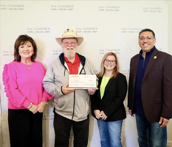 four people posing for a picture holding a big check