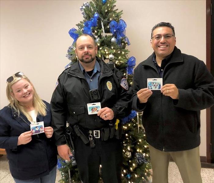 Two people posing with a cop while holding gift cards.