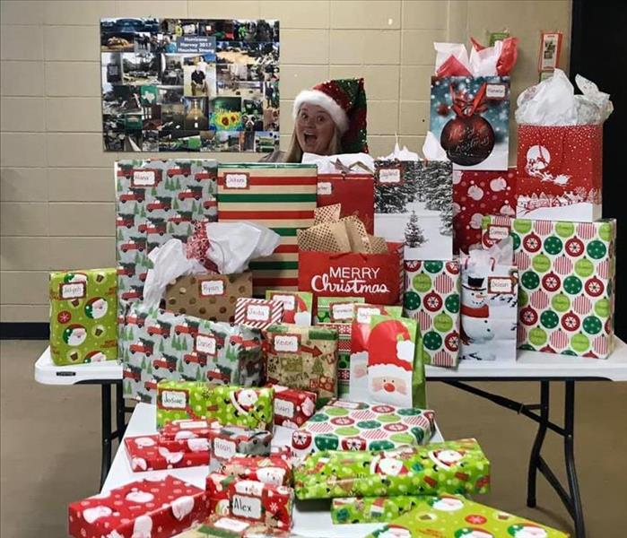 A woman standing behind a large amount of presents stacked on top of eachother.