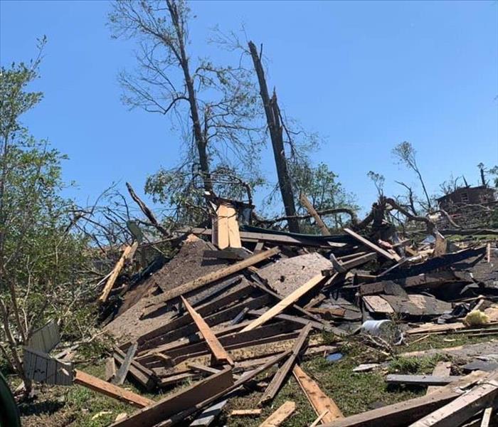 A destroyed house with trees and debris scattered across the home.