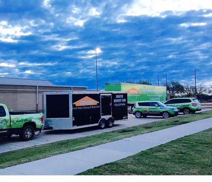 SERVPRO vehicles parked in a line outside of a school.