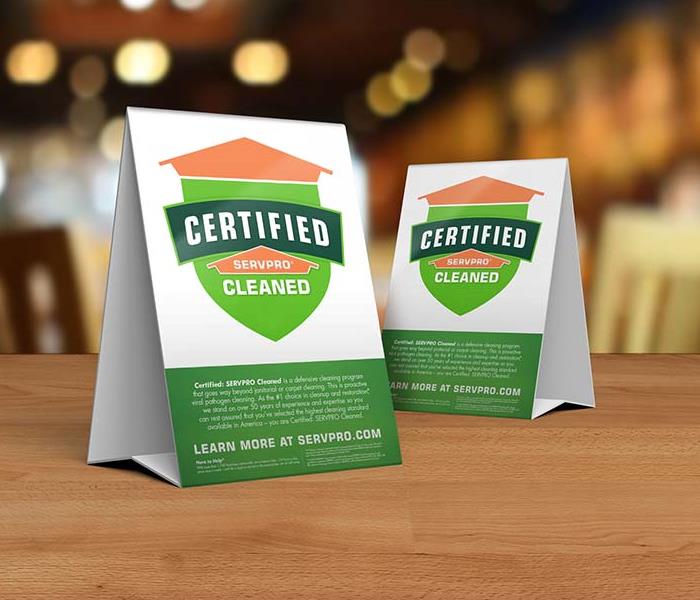 Table tent signs describing the Certified: SERVPRO Cleaned program on top of a wooden table.