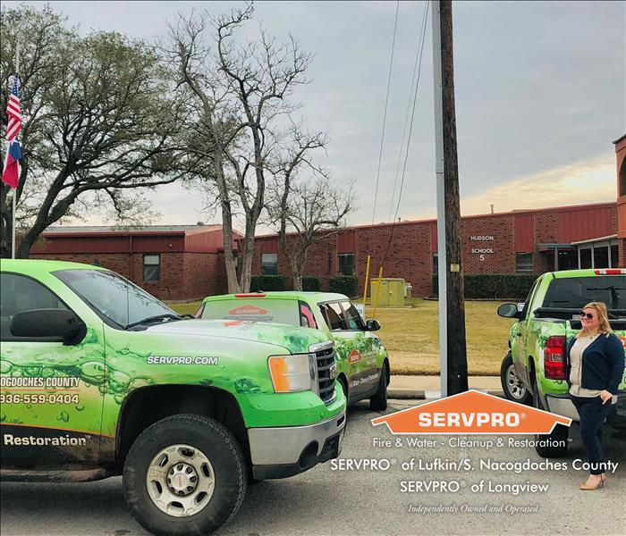 SERVPRO female employee stands with SERVPRO vehicles in front of business