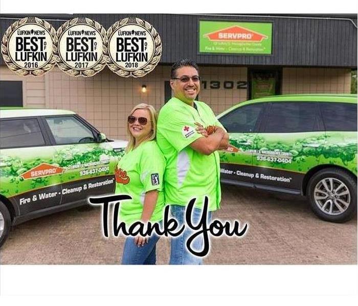 Two people standing back to back in front of SERVPRO vehicles